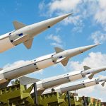 Multiple missiles pointed upward on launchers against blue sky.