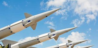 Multiple missiles pointed upward on launchers against blue sky.