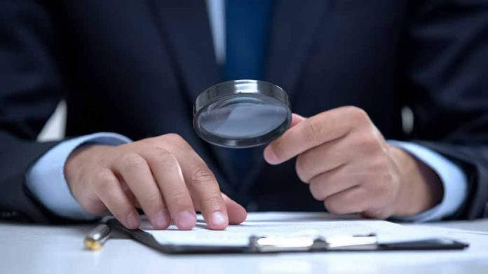 Man holding magnifying glass, examining document on clipboard.