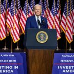 President Joe Biden speaks behind podium with American flags.