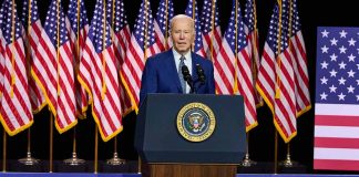 President Joe Biden speaks behind podium with American flags.