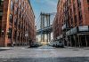 Street view with bridge between two brick buildings.