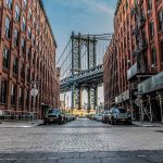 Street view with bridge between two brick buildings.