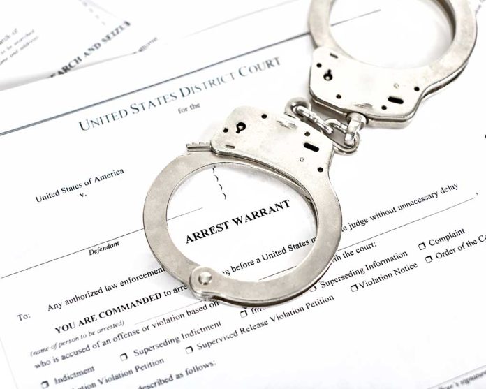 Handcuffs on top of an arrest warrant document.