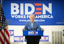 Man at podium with Biden campaign signs behind him.