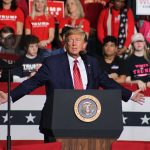 Person speaking at podium with crowd behind them.