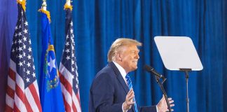 Person speaking at podium with flags in background.