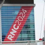 Building with "RNC 2024" sign, red construction cranes.