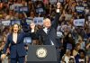 Two people celebrate on stage with supporters behind.