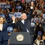 Two people celebrate on stage with supporters behind.