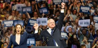 Two people celebrate on stage with supporters behind.