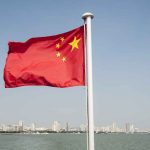 Chinese flag waving over cityscape and water.