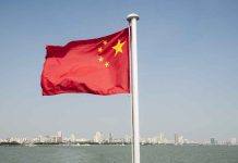 Chinese flag waving over cityscape and water.