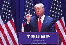 Person speaking at podium with multiple American flags.