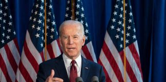 Man speaking at podium with American flags behind.