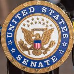 US Senate emblem with microphones in background.