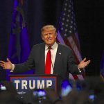 Man speaking at podium with flags behind him.