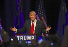 Man speaking at podium with flags behind him.