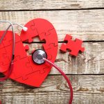 Red heart puzzle with stethoscope on wooden background.