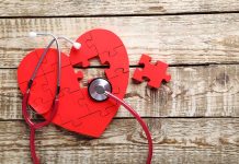 Red heart puzzle with stethoscope on wooden background.