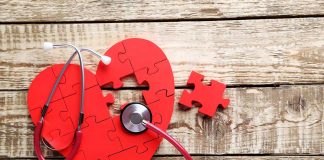 Red heart puzzle with stethoscope on wooden background.