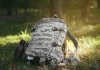 Camouflage backpack and canteen beside a tree.