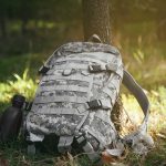 Camouflage backpack and canteen beside a tree.