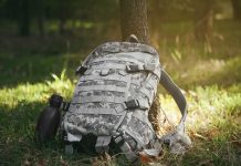 Camouflage backpack and canteen beside a tree.