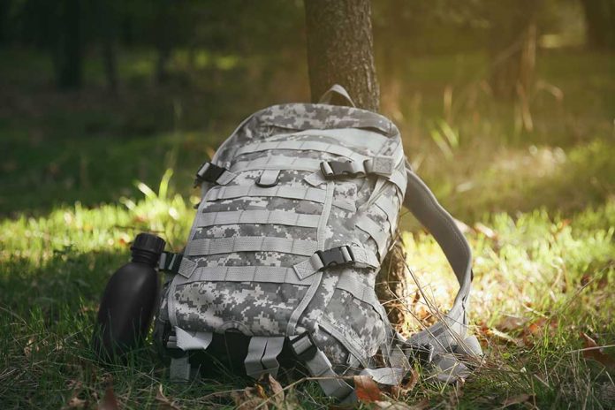 Camouflage backpack and canteen beside a tree.