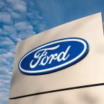 Ford logo sign against blue sky.