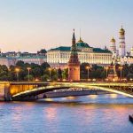 Illuminated bridge and Kremlin complex across river at twilight.