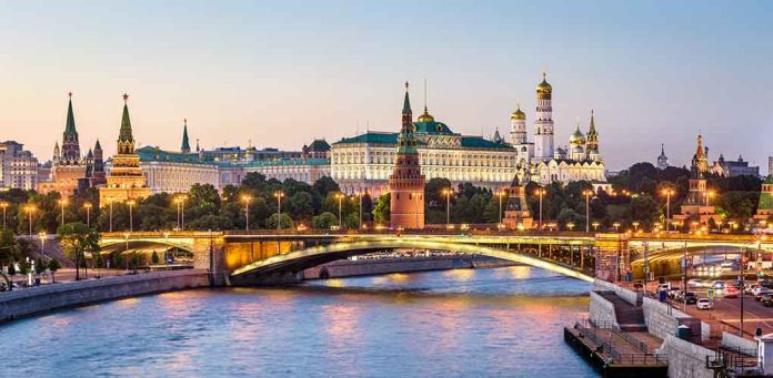 Illuminated bridge and Kremlin complex across river at twilight.