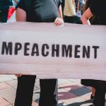 Person holding an "Impeachment" sign at protest.