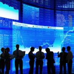 Silhouetted people in front of stock market displays.