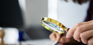 Person examining document with magnifying glass.