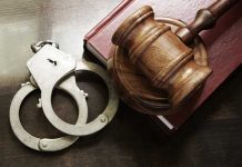 Gavel, handcuffs, and book on wooden surface.