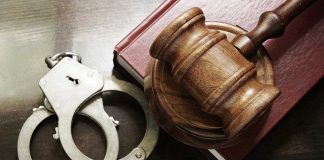 Gavel, handcuffs, and book on wooden surface.