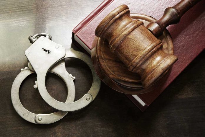 Gavel, handcuffs, and book on wooden surface.