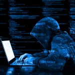 Hooded figure using laptop with code background.