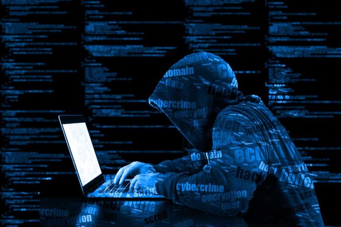 Hooded figure using laptop with code background.