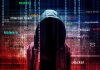 Hooded figure with digital security terms background.