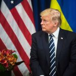 Man in suit sitting near US and Ukrainian flags