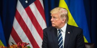 Man in suit sitting near US and Ukrainian flags