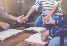 People holding hands in prayer with open books