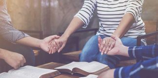 People holding hands in prayer with open books