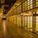 Empty hallway between rows of prison cells.