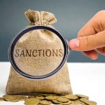 Hand holding magnifying glass over sack labeled "Sanctions".