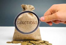 Hand holding magnifying glass over sack labeled "Sanctions".