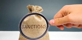 Hand holding magnifying glass over sack labeled "Sanctions".