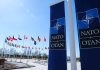 NATO flags and banners under clear sky.